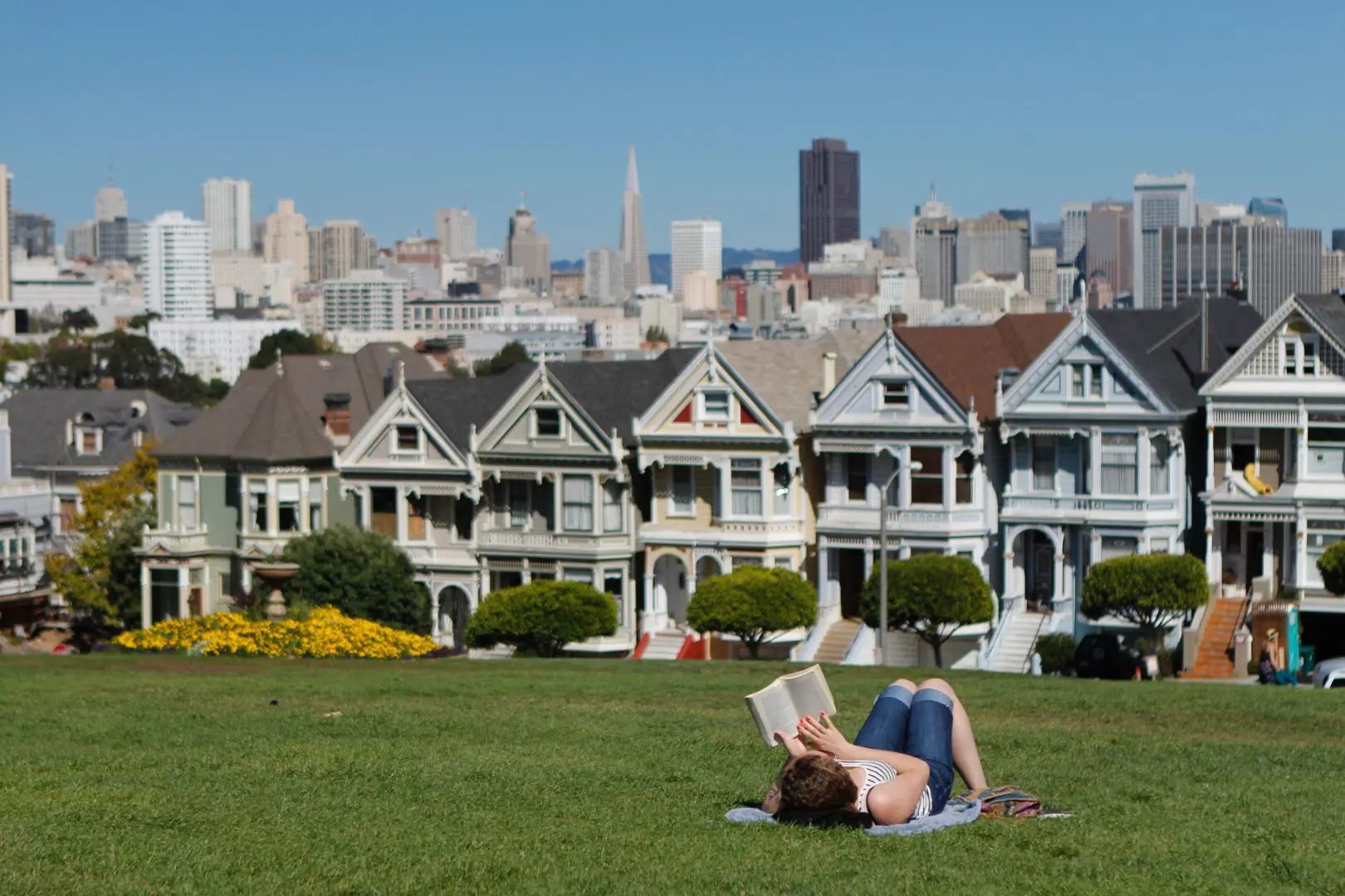 A person reads on the grass in front of some houses.